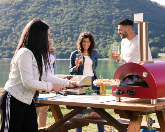 group of people cooking a meal using a portable oven near a lake and mountain