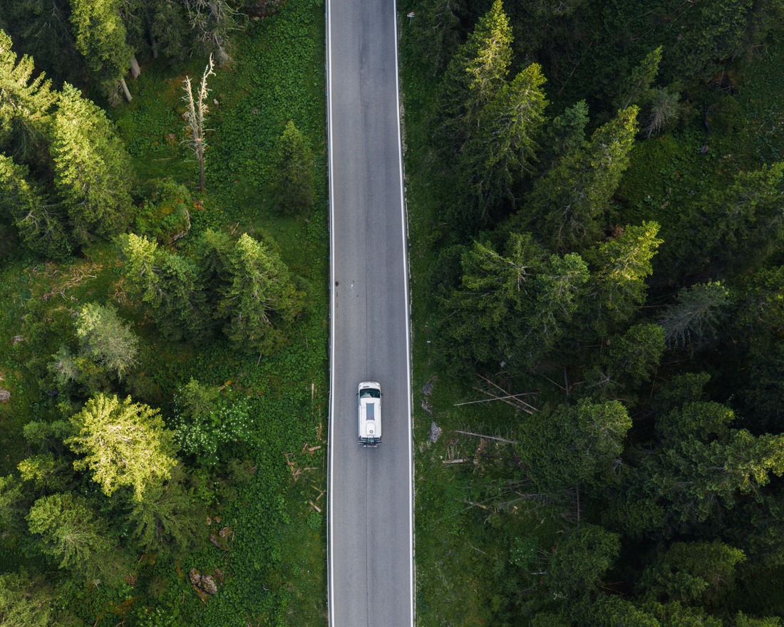 van life van traveling on a straight road with green trees on each side.