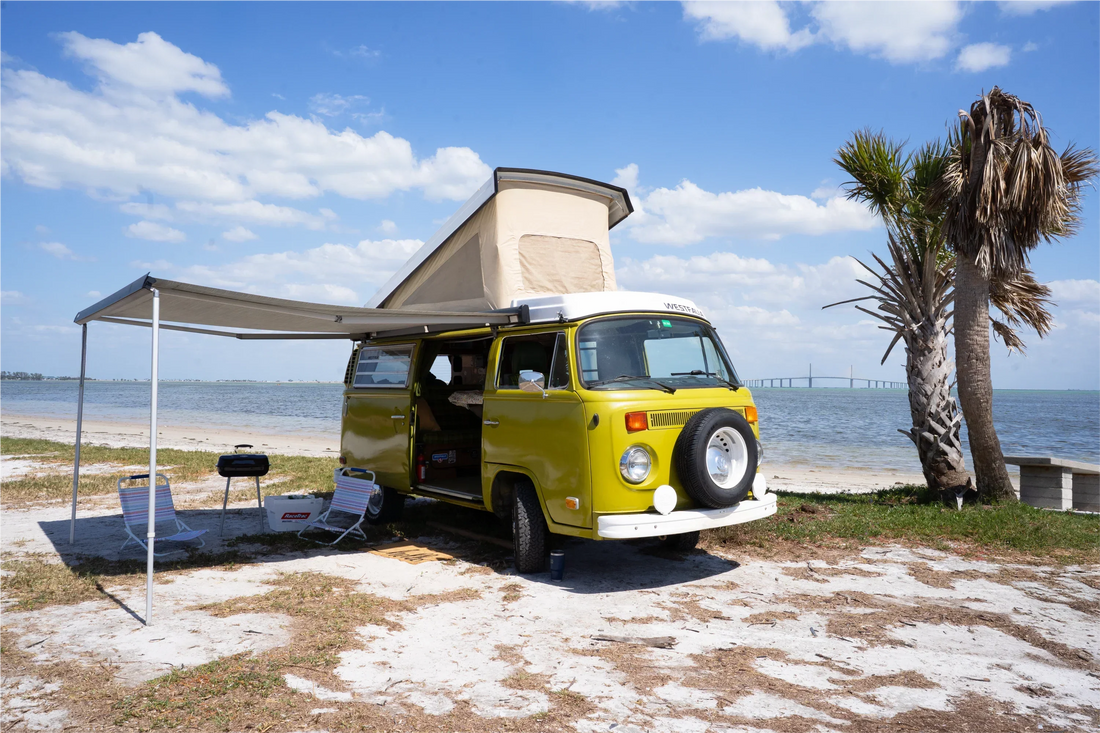 vanlife kiwi volkwagen van with opened door parked at the beach on a sunny day with shelter extending from the side