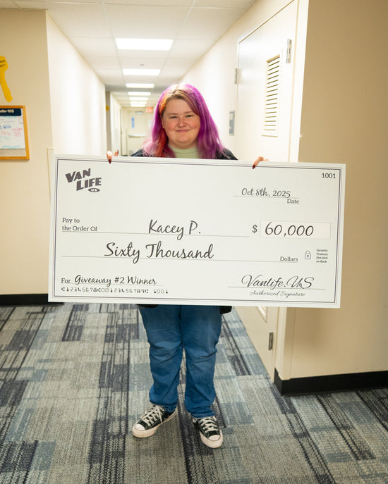VanLife Mango Winner Kacey P standing in hallway holding up a $60,000 check from vanlife.us.