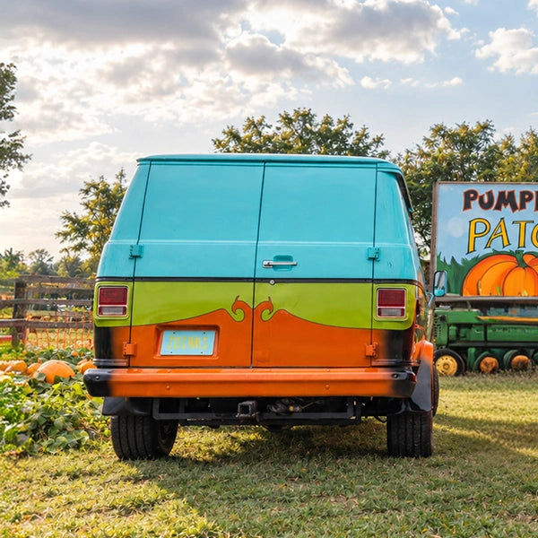 The rear of the teal, green and orange van parked on grass at a pumpkin patch
