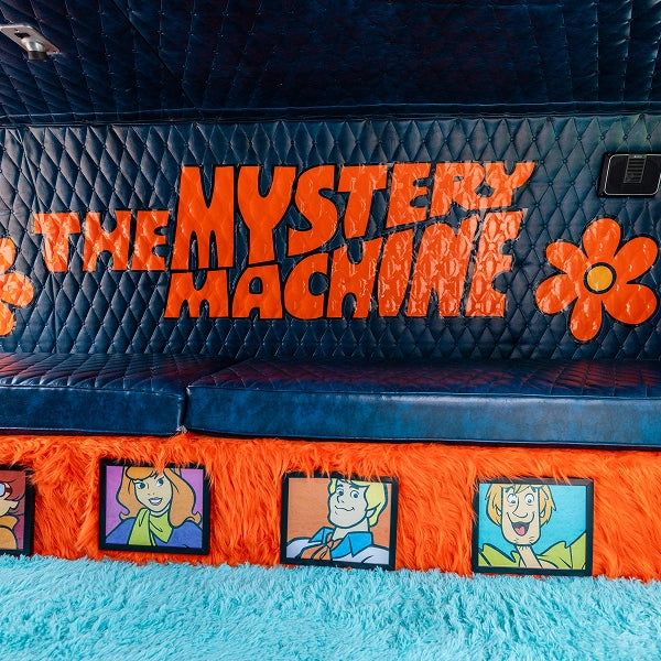 The quilted rear bench above orange shag, with framed cartoon-style portraits and teal carpet