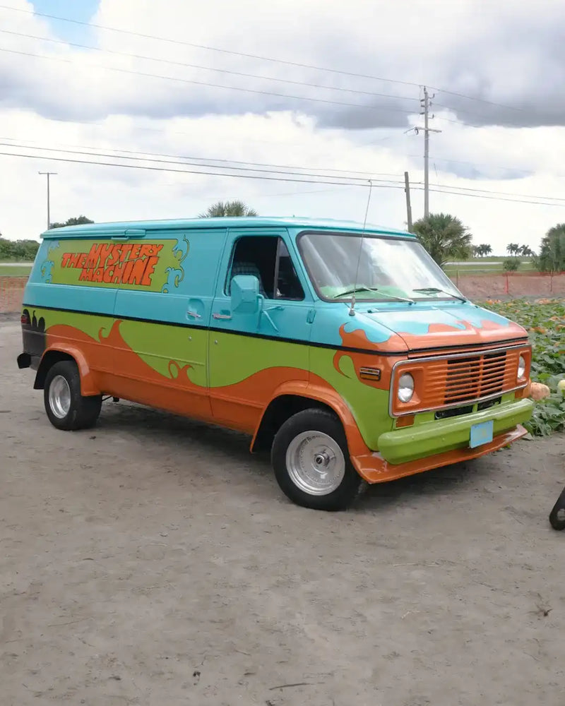 The custom van parked on a dirt lot, showing its teal roof, green body stripe and orange lower graphics