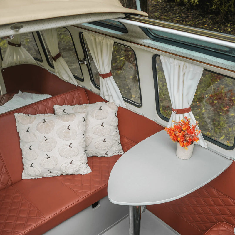 Inside the prize Bus: a rust-orange diamond-stitched bench with pumpkin-print pillows, a white table and curtained windows